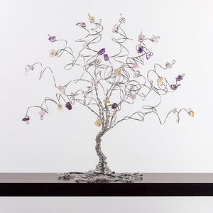 May include: A silver wire tree sculpture with purple, pink, and yellow gemstones attached to the branches.