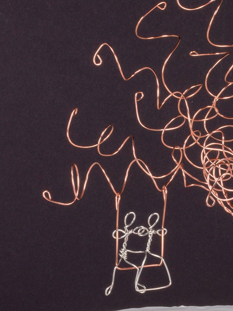 May include: A wire sculpture of a tree with two figures on a swing. The tree is made of copper wire and the figures are made of silver wire.
