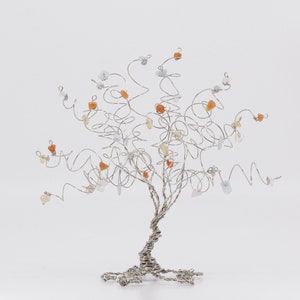 May include: A silver wire tree sculpture with a twisted trunk and branches adorned with small, colorful gemstones. The gemstones are in shades of orange, yellow, and blue.