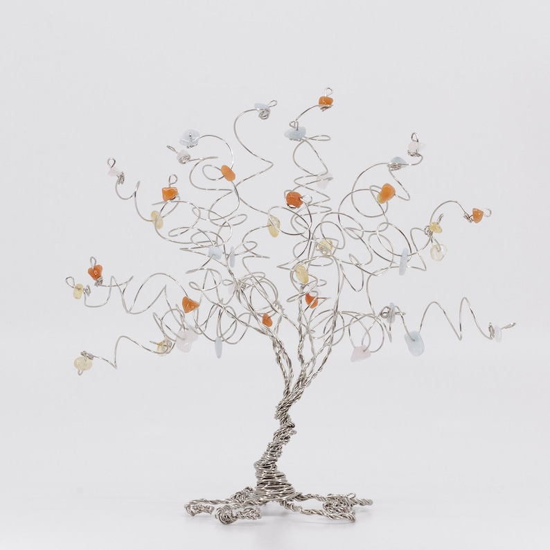 May include: A silver wire tree sculpture with a twisted trunk and branches adorned with small, colorful gemstones. The gemstones are in shades of orange, yellow, and blue.
