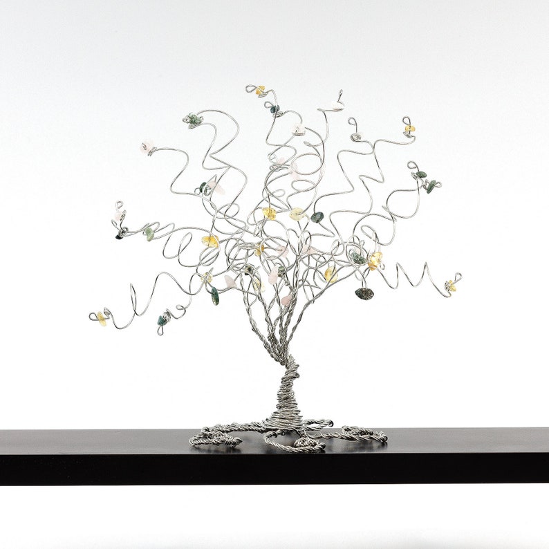 May include: A silver wire tree sculpture with a twisted trunk and branches adorned with colorful gemstones. The tree is displayed on a black shelf.