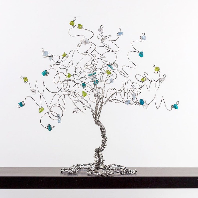 May include: A silver wire tree sculpture with blue, green, and clear glass beads. The tree is on a dark brown surface.