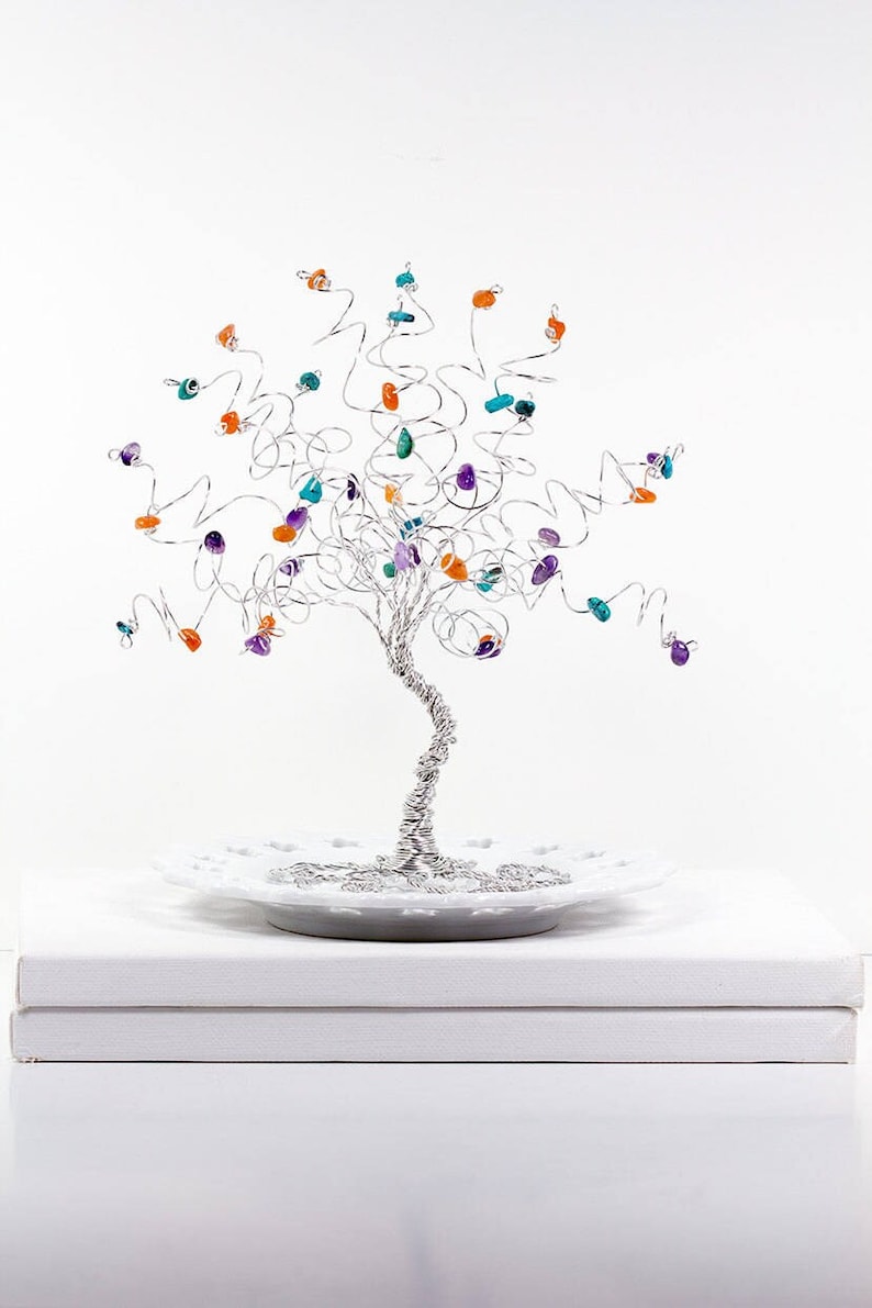 May include: A silver wire tree sculpture with colorful gemstones. The tree is on a white plate and a white base.