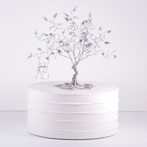 May include: A white cake with a silver wire tree topper decorated with blue and purple beads. The tree topper is a wedding cake topper.