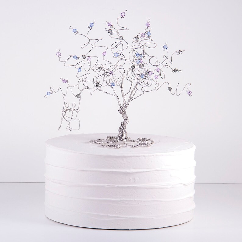 May include: A white cake with a silver wire tree topper decorated with blue and purple beads. The tree topper is a wedding cake topper.