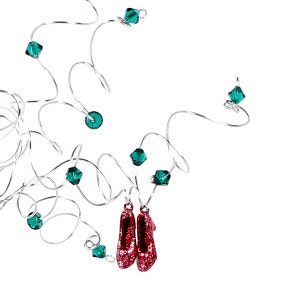 May include: A pair of red glitter shoes with emerald green crystal accents hanging from a silver wire.