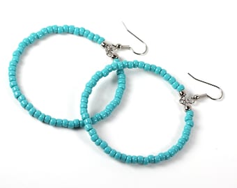 May include: A pair of turquoise blue hoop earrings made of small beads. The earrings have silver hooks.