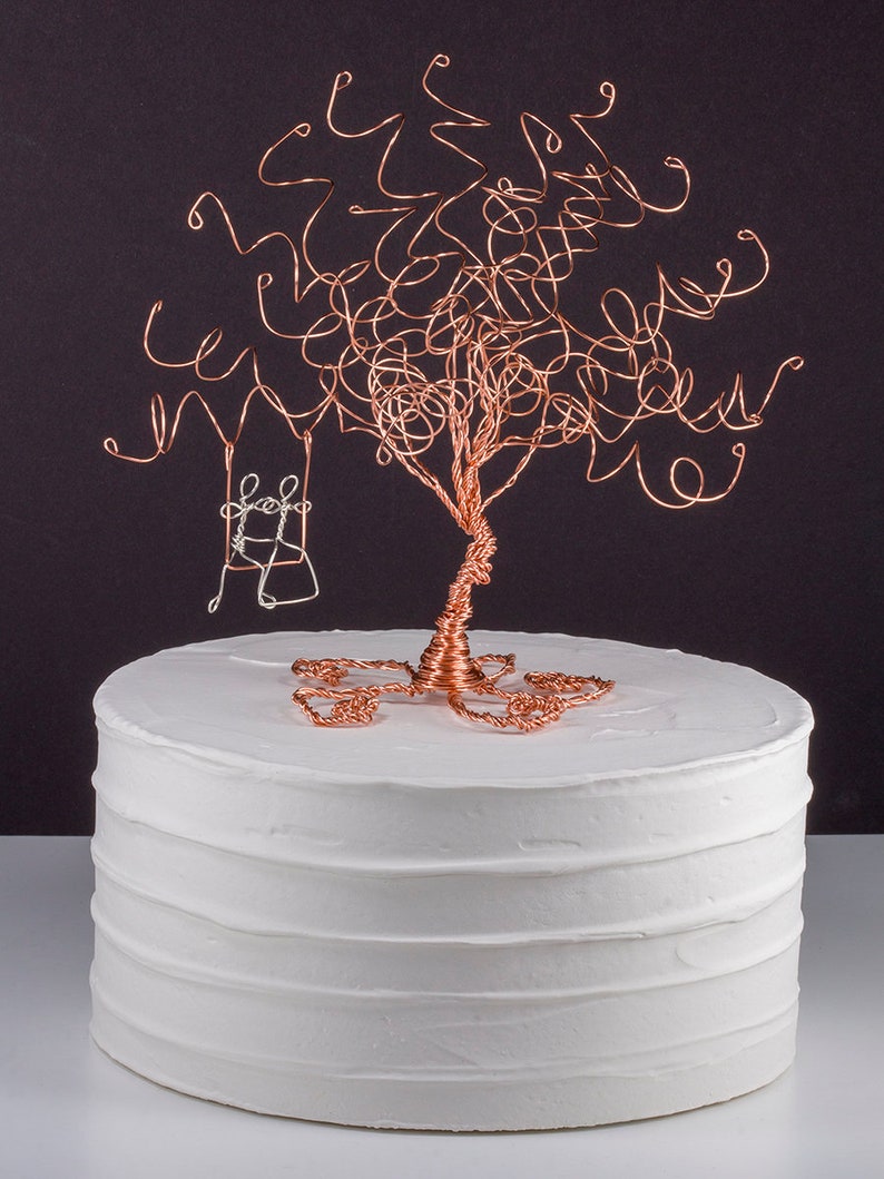 May include: A white cake with a copper wire tree topper. The tree has a small swing hanging from it.