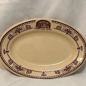 May include: Oval-shaped cream-colored platter with a brown border featuring repeating decorative elements. The platter has a central image and text that reads "Silver Castle System" in brown.