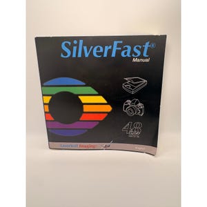 Può includere: Un manuale SilverFast nero con testo blu e un grafico circolare color arcobaleno. La copertina presenta disegni al tratto bianchi di uno scanner e di una fotocamera, il testo 48 Bit e il logo LaserSoft Imaging nella parte inferiore.