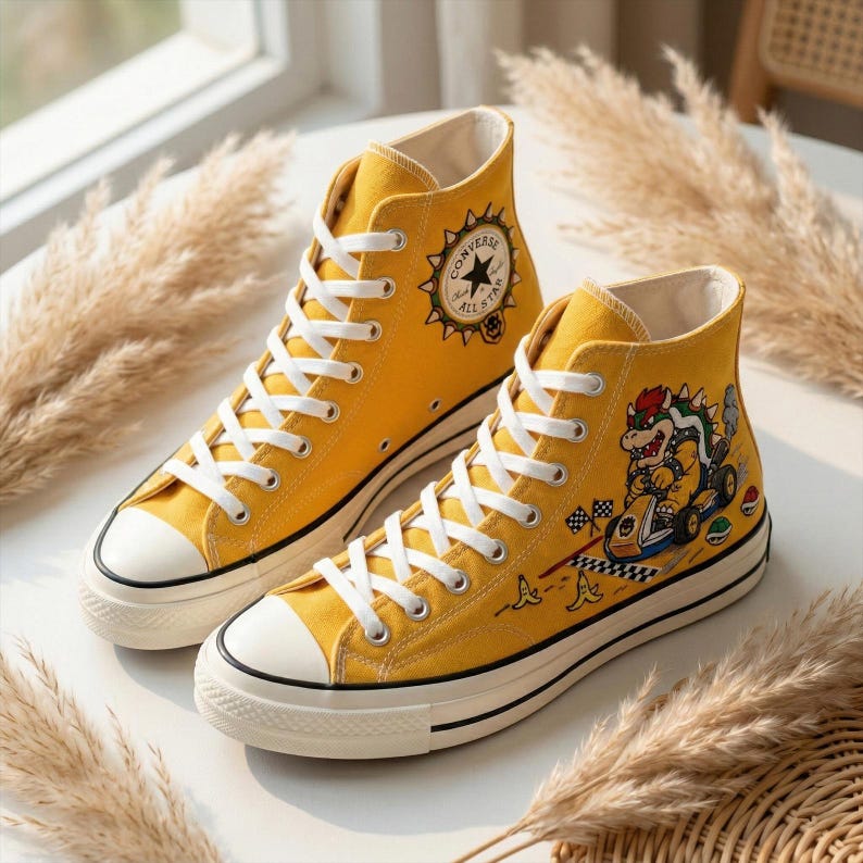 Puede incluir: Un par de zapatillas Converse All Star altas amarillas con cordones blancos y puntera blanca. Un zapato presenta un gr&aacute;fico de Bowser. El logotipo de Converse est&aacute; en el lateral. Los zapatos est&aacute;n sobre una superficie blanca.