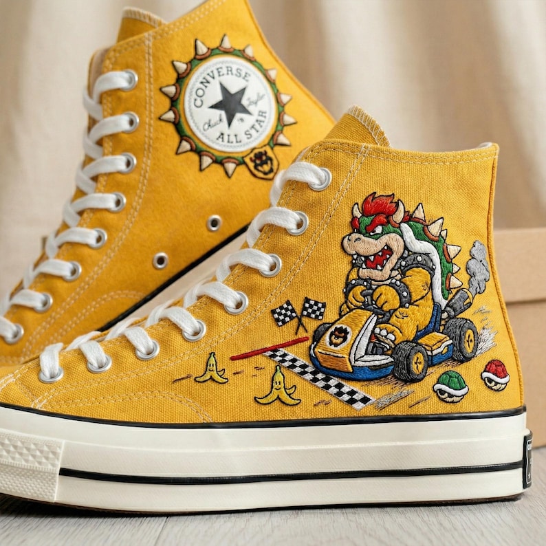 Puede incluir: Zapatillas altas de color amarillo mostaza con cordones y suelas blancas. Las zapatillas presentan un dise&ntilde;o del personaje Bowser en el lateral, con detalles de banderas a cuadros y c&aacute;scaras de pl&aacute;tano. El logo de Converse All Star est&aacute; en el tobillo.