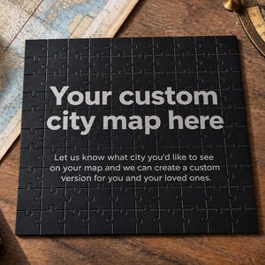 Può includere: Un puzzle quadrato nero con il testo bianco "Your custom city map here" seguito da "Let us know what city you'd like to see on your map and we can create a custom version for you and your loved ones."