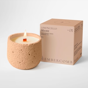 May include: A lit, peach-coloured candle in a textured ceramic container, with a wooden wick. The candle is next to a matching box that reads "Limoncello Bloom" and "Pure Organic Lemon Essential Oil". The candle is 255g.