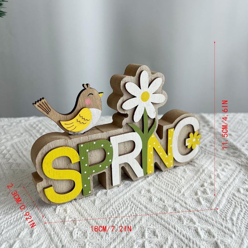 Puede incluir: Decoraci&oacute;n de primavera de madera con un p&aacute;jaro y una flor. La palabra "SPRING" est&aacute; escrita en letras blancas, amarillas y verdes. La decoraci&oacute;n mide 18 cm de largo, 11,5 cm de alto y 2,3 cm de grosor.