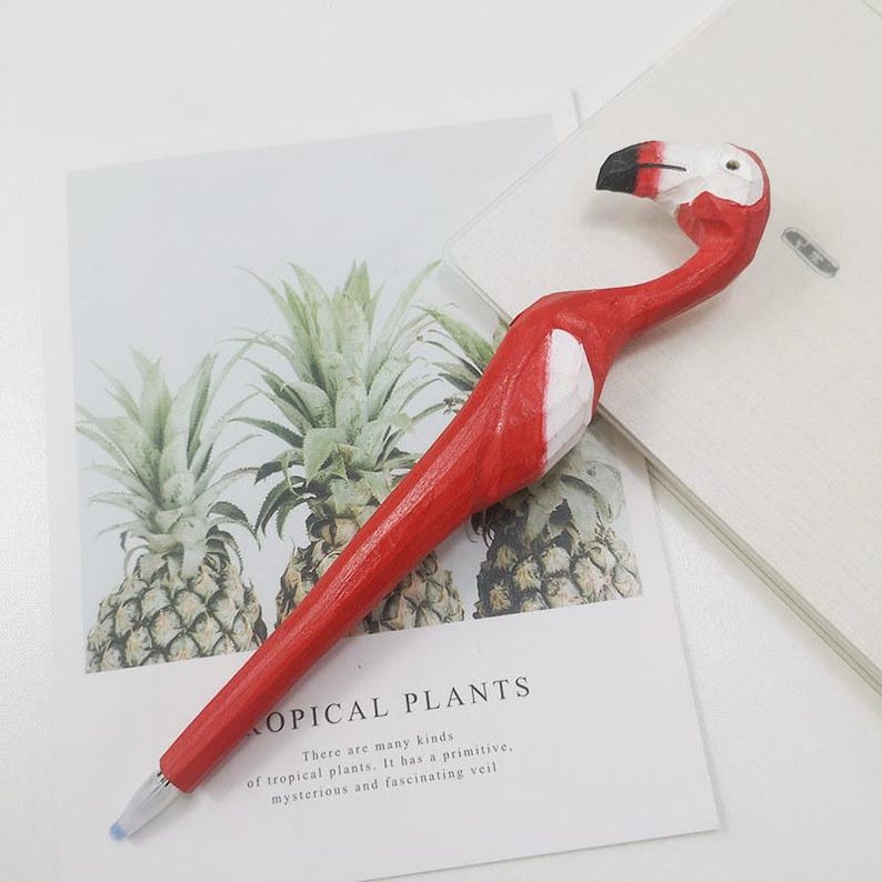Puede incluir: Un bol&iacute;grafo rojo con forma de flamenco con pico blanco y negro. El bol&iacute;grafo est&aacute; sobre una superficie blanca con una tarjeta que dice "TROPICAL PLANTS". El bol&iacute;grafo es un instrumento de escritura &uacute;nico.