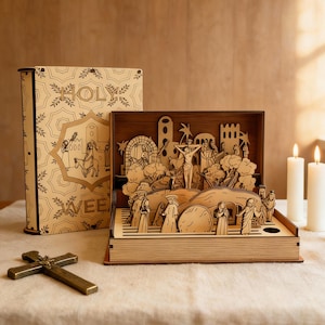 May include: A wooden religious diorama depicting a biblical scene, featuring figures, structures, and a cross. A decorative book with the word "HOLY" and "WEE" is behind the diorama. A brass cross and two lit candles are in the foreground.