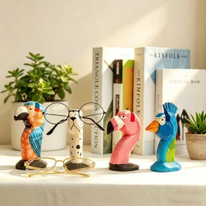 May include: A collection of four colorful, hand-carved wooden eyeglass holders. The holders are shaped like a parrot, a dog, a flamingo, and a blue bird. Each holder has a black base and is designed to hold a pair of glasses. The glasses are not included.