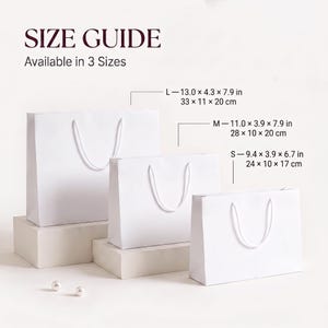 May include: Three plain white paper gift bags with white cord handles, displayed in small, medium, and large sizes. Text reads SIZE GUIDE Available in 3 Sizes. Dimensions are listed as L 33 x 11 x 20 cm, M 28 x 10 x 20 cm, and S 24 x 10 x 17 cm.