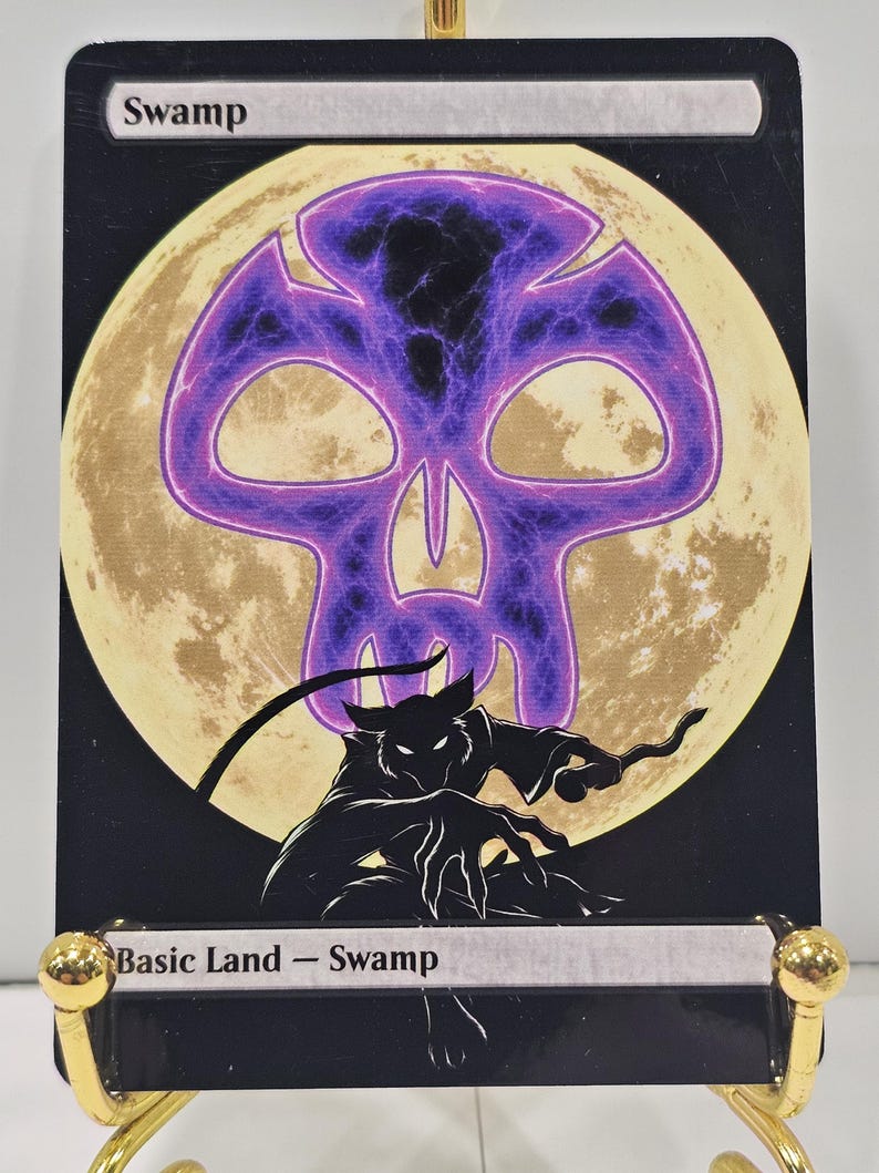Op de afbeelding: Een rechthoekige ruilkaart met de titel Swamp, met een groot, gloeiend paars schedelpictogram gecentreerd over een lichtgele volle maan. Onder de maan staat een zwart silhouet van een gebogen, klauwend wezen tegen een donkere achtergrond. De tekst luidt Swamp en Basic Land - Swamp.