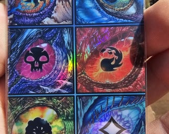 Op de afbeelding: Een rechthoekige kaart met zes kleurrijke oogontwerpen. Elk oog heeft een uniek kleurenschema en symbool, waaronder een zon, een waterdruppel, een schedel, een vlam, een boom en een ruit. De kaart heeft een holografische glans.