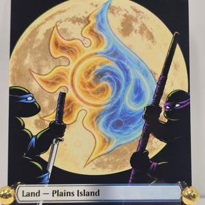 May include: A rectangular trading card titled Tundra featuring a large yellow moon background. Two green turtle characters are depicted in silhouette, one holding a sword and the other a staff, flanking a central swirling orange and blue energy symbol.