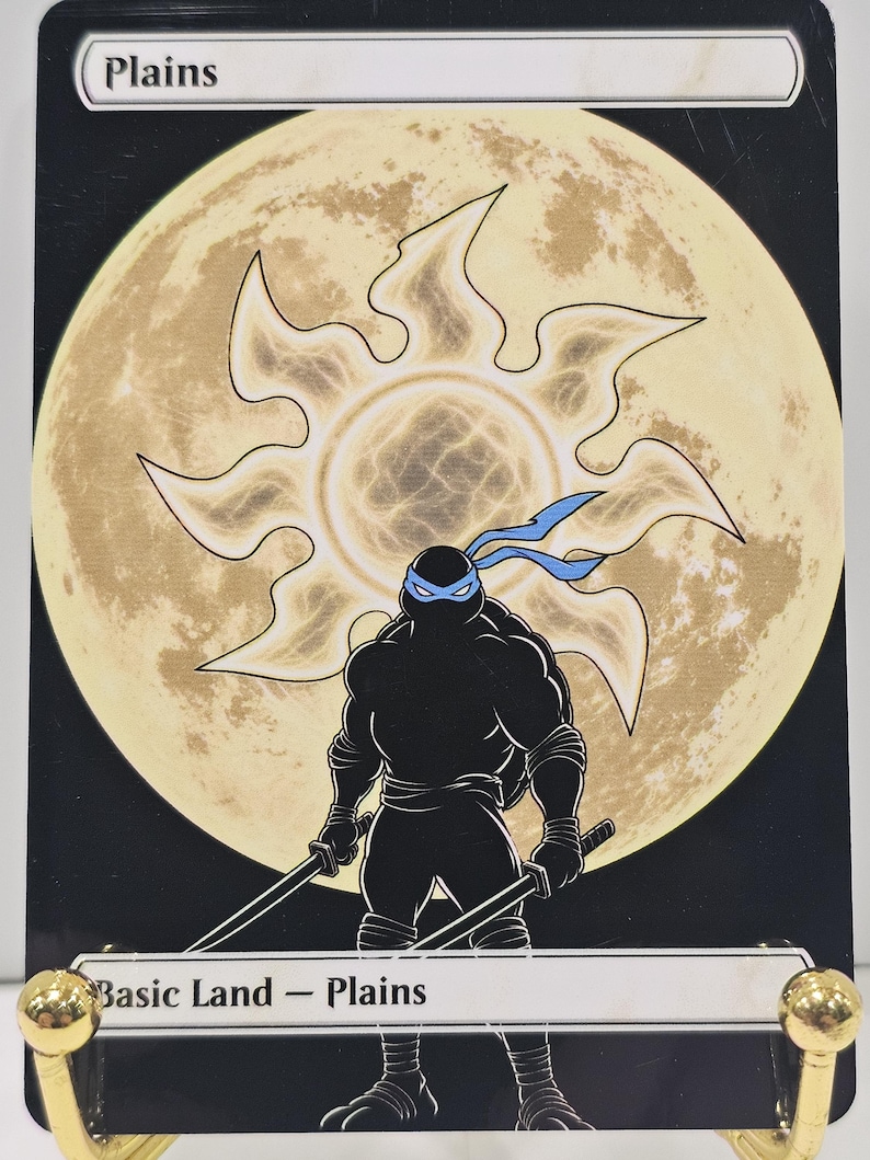 Op de afbeelding: Een rechthoekige ruilkaart met de titel Plains, voorzien van een zwart silhouet van een schildpadfiguur met een blauw masker en twee zwaarden. Achter het personage staat een groot, lichtgeel zonicoon tegen een zwarte achtergrond.
