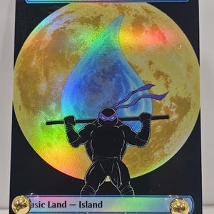 Op de afbeelding: Een rechthoekige ruilkaart met een holografische afwerking met een grote gele maan en een blauw waterdruppelpictogram. Een zwart silhouet van een ninja met een paars masker houdt een staf vast. De tekst Island staat aan de boven- en onderkant.