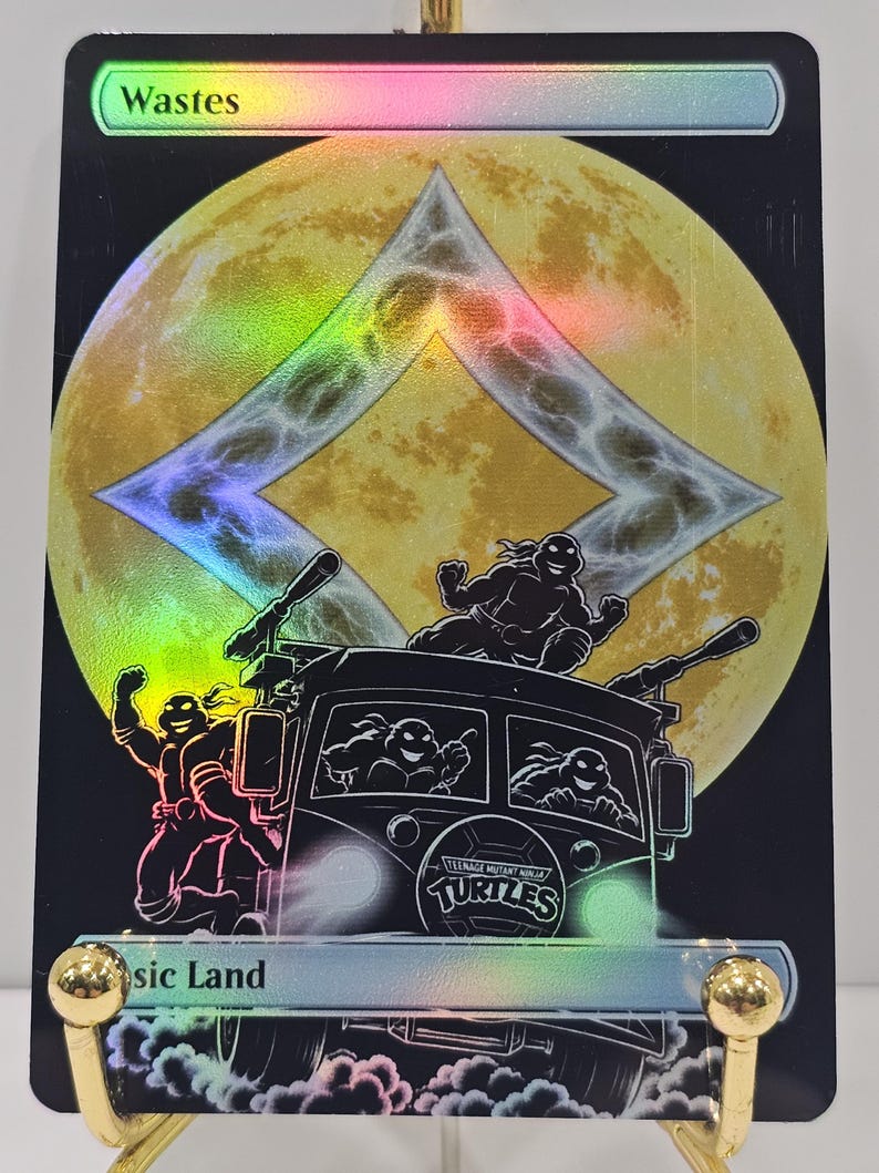 Op de afbeelding: Een holografische ruilkaart getiteld Wastes, met een grote gele maan achter een ruitvormig symbool. Daaronder staan de Teenage Mutant Ninja Turtles afgebeeld in hun busje, met &eacute;&eacute;n schildpad op het dak en twee zichtbaar door de voorruit.