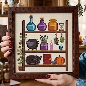 May include: A cross-stitch embroidery in a dark wood frame featuring three shelves. The shelves hold blue, purple, and orange potion bottles, an hourglass, a black cauldron, herbs, a crystal, a sleeping black cat, a red book, and a pumpkin.