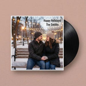 Puede incluir: Un disco de vinilo negro con una portada cuadrada. La portada muestra a una pareja sentada en un banco en una escena nevada, con el texto "Happy Holidays! The Smiths". Se ven luces de hadas en el fondo.