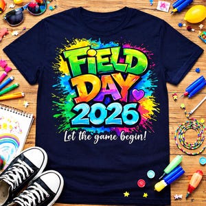 May include: Navy blue t-shirt with a colorful "Field Day 2026" graphic. The design features vibrant text and a heart, with the phrase "Let the game begin!" below. The shirt is surrounded by school supplies.