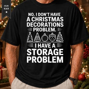 Puede incluir: Una camiseta negra de manga corta con texto blanco que dice: NO, I DON'T HAVE A CHRISTMAS DECORATIONS PROBLEM. I HAVE A STORAGE PROBLEM. Entre las líneas de texto hay iconos de líneas blancas de tres árboles de Navidad y dos adornos.
