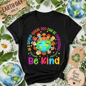 May include: Black t-shirt with a vibrant graphic. It features a globe encircled by children of different ethnicities, with the text "In a world where you can be everything, Be Kind." The shirt also has "Earth Day April 22" printed on it.