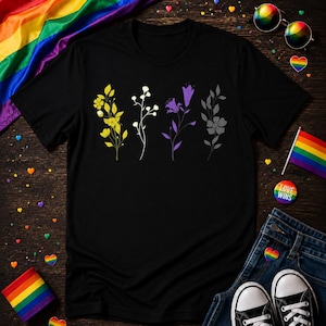 May include: Black t-shirt featuring a floral design in yellow, white, purple, and gray. The shirt is surrounded by rainbow-themed accessories, including a flag, sunglasses, and heart-shaped pins. A pair of black and white sneakers and denim shorts are also visible.