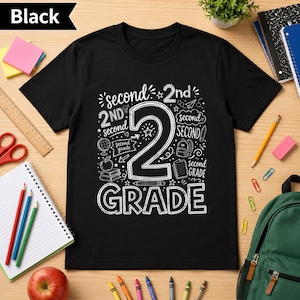 Può includere: Una t-shirt nera a maniche corte con un design grafico bianco che mostra il grande numero 2 e il testo second grade. Il design include varie illustrazioni a tema scolastico come un mappamondo, una mela, libri, uno zaino e delle matite.