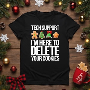 Może przedstawiać: Czarny t-shirt z białym napisem "TECH SUPPORT I'M HERE TO DELETE YOUR COOKIES". Projekt zawiera grafikę ludzika z piernika, choinki, dzwonka i gwiazdy. Świąteczna odzież.