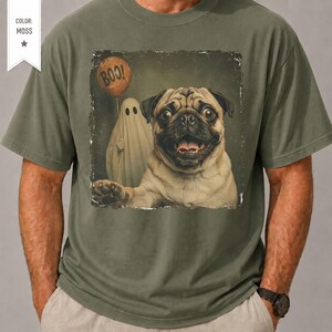 Könnte beinhalten: Ein moosgrünes T-Shirt mit einem Grafikdruck eines Mopses mit weit aufgerissenen Augen und offenem Maul. Neben dem Hund befindet sich eine weiße Geisterfigur, die einen orangefarbenen Luftballon mit dem schwarzen Aufdruck BOO! hält.