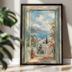 Op de afbeelding: Een ingelijste muurkunstprint met een uitzicht vanuit een open raam op een mediterrane kuststad. De scène toont lichtblauwe houten luiken, een terracotta plantenpot op een balkon, witte gebouwen met blauwe koepels en de blauwe zee.