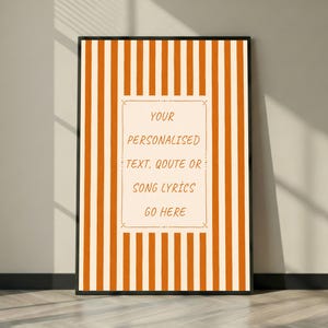 Peut inclure: Une affiche encadrée avec une bordure noire, ornée de rayures verticales orange et crème. Le centre présente un encadré rectangulaire crème avec le texte "YOUR PERSONALISED TEXT, QUOTE OR SONG LYRICS GO HERE".