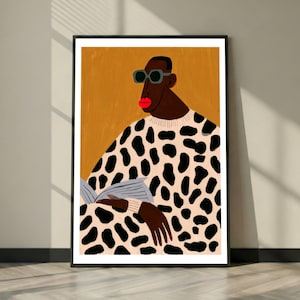 Könnte beinhalten: Ein gerahmter Kunstdruck mit einer stilisierten Illustration einer Person mit dunkler Haut, leuchtend roten Lippen und einer dunklen Sonnenbrille. Die Person trägt einen cremefarbenen Pullover mit schwarzem Leopardenmuster und hält ein offenes graues Buch.