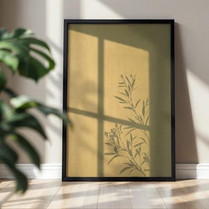 Puede incluir: Una impresión de arte mural rectangular en un marco negro fino. La obra presenta un fondo amarillo mostaza sólido con la silueta oscura de una rama frondosa proyectada en el centro, superpuesta por un patrón de sombra de ventana en cuadrícula.