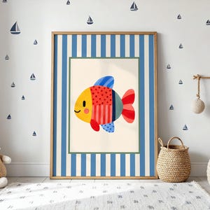 Può includere: Una stampa artistica da parete rettangolare incorniciata raffigurante un pesce stilizzato con testa gialla, sezione centrale a pois rossi e coda a righe rosse. La stampa è su sfondo crema, racchiusa da un bordo a righe verticali blu e bianche.
