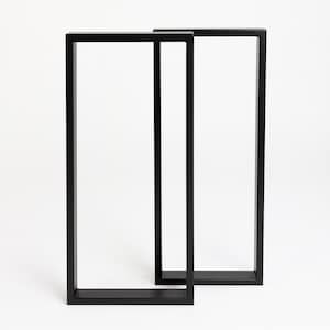 Peut inclure: Deux pieds de table en métal noir de forme rectangulaire. Les pieds sont en métal robuste et sont conçus pour supporter un plateau de table. Les pieds sont présentés sur fond blanc.