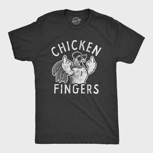 Puede incluir: Camiseta gris oscuro con un gráfico blanco desgastado de un pollo con gafas de sol haciendo una peineta. El texto "CHICKEN FINGERS" está arriba y abajo de la imagen.
