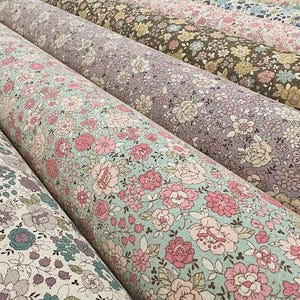 以下が含まれることがあります： さまざまな花の模様が施された生地のロールのクローズアップ。生地は、ピンク、青、紫、茶色の色合いで、さまざまな花のパターンが特徴です。ロールはしっかりと巻かれており、生地の複雑なデザインと質感を表現しています。