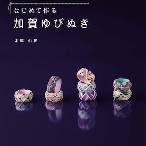 May include: A book cover with Japanese text and several colourful, patterned finger rings. The rings are stacked and arranged on a dark purple surface. The book title is "Kaga Yubinuki".