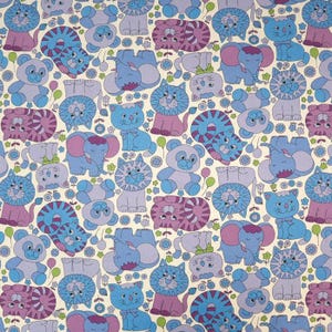May include: A repeating pattern fabric featuring cartoon cats, elephants, and bears in shades of blue, purple, and lavender on a cream background. The design includes small green and blue flowers and balloons scattered between the animal figures.