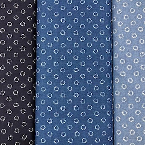 May include: Three fabric swatches in varying shades of blue. Each swatch features a repeating pattern of small white floral-like designs. The fabrics range from a deep navy to a light, almost sky blue, creating a visually appealing contrast.