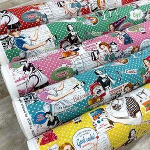 Może przedstawiać: Zrolowane bele materiału z nadrukami w stylu retro kuchni. Wzory obejmują grochy, ilustracje kobiet gotujących i tekst, np. "Cooking Recipes". Kolory to czerwony, zielony, różowy, turkusowy i żółty.